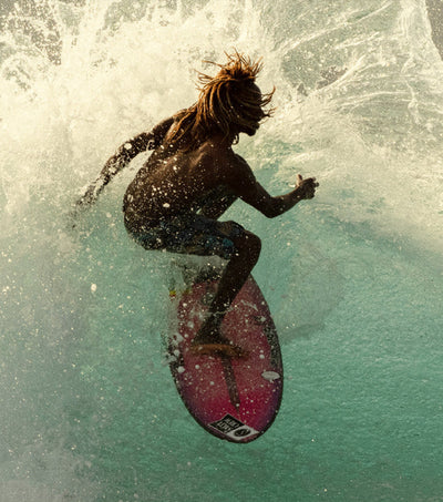Surfer catching air off a wave at golden hour, showcasing the energy of the Discover Ambassador Collection - Sun Bum.