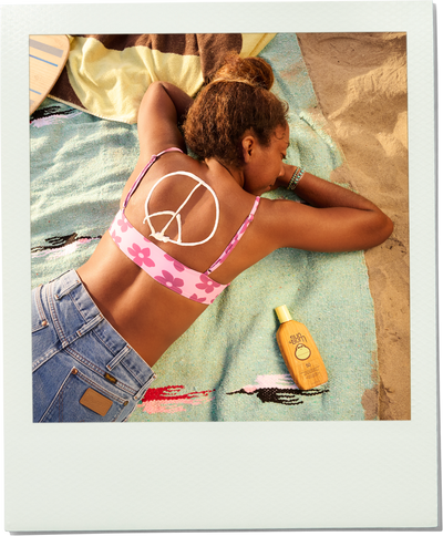 Woman in a bikini lying on a towel with a sun screen bottle next to her at the beach.